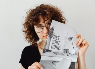 Kobieta w okularach trzyma plakat Get Shit Done jako motywację