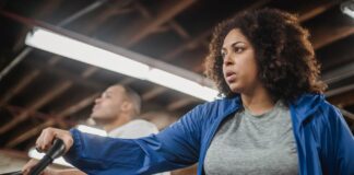Zestresowana kobieta plus size na rowerku stacjonarnym obok wysportowanego mężcz